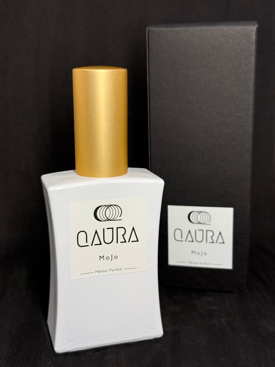 QAURA Mental Parfuem MoJo steht neben der schwarzen Verpackung auf einem Holz-Untergrund.